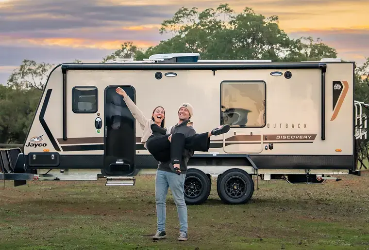 A couple celebrating in front of a Jayco caravan at sunset